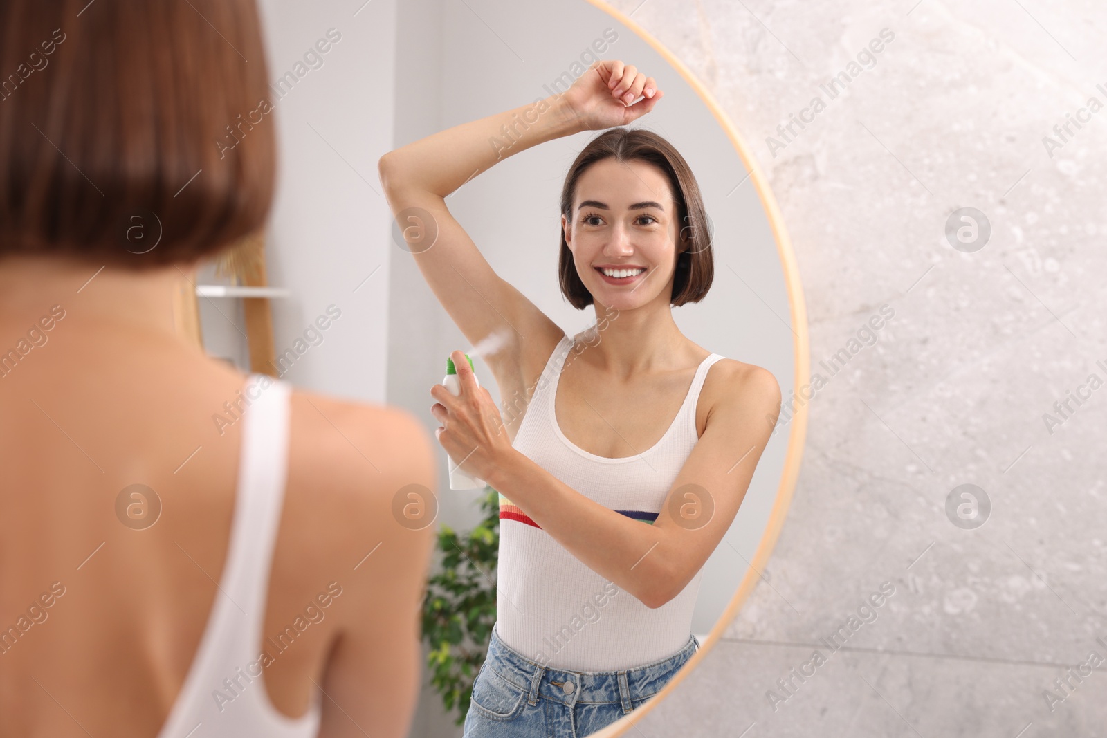 Photo of Smiling woman applying spray deodorant near mirror at home