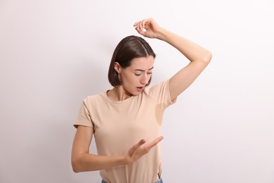 Emotional woman in t-shirt before using deodorant on white background