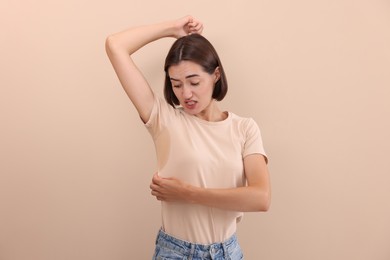 Emotional woman in t-shirt before using deodorant on beige background