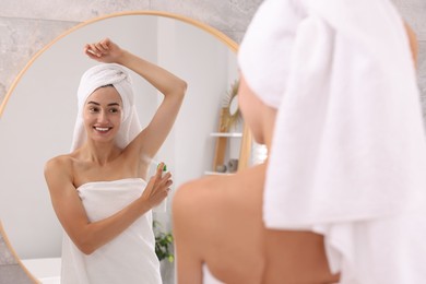 Photo of Smiling woman applying spray deodorant near mirror at home, back view