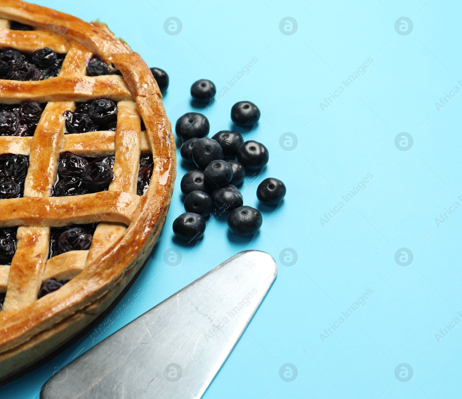 Photo of Tasty homemade pie with blueberries and server on light blue table, closeup