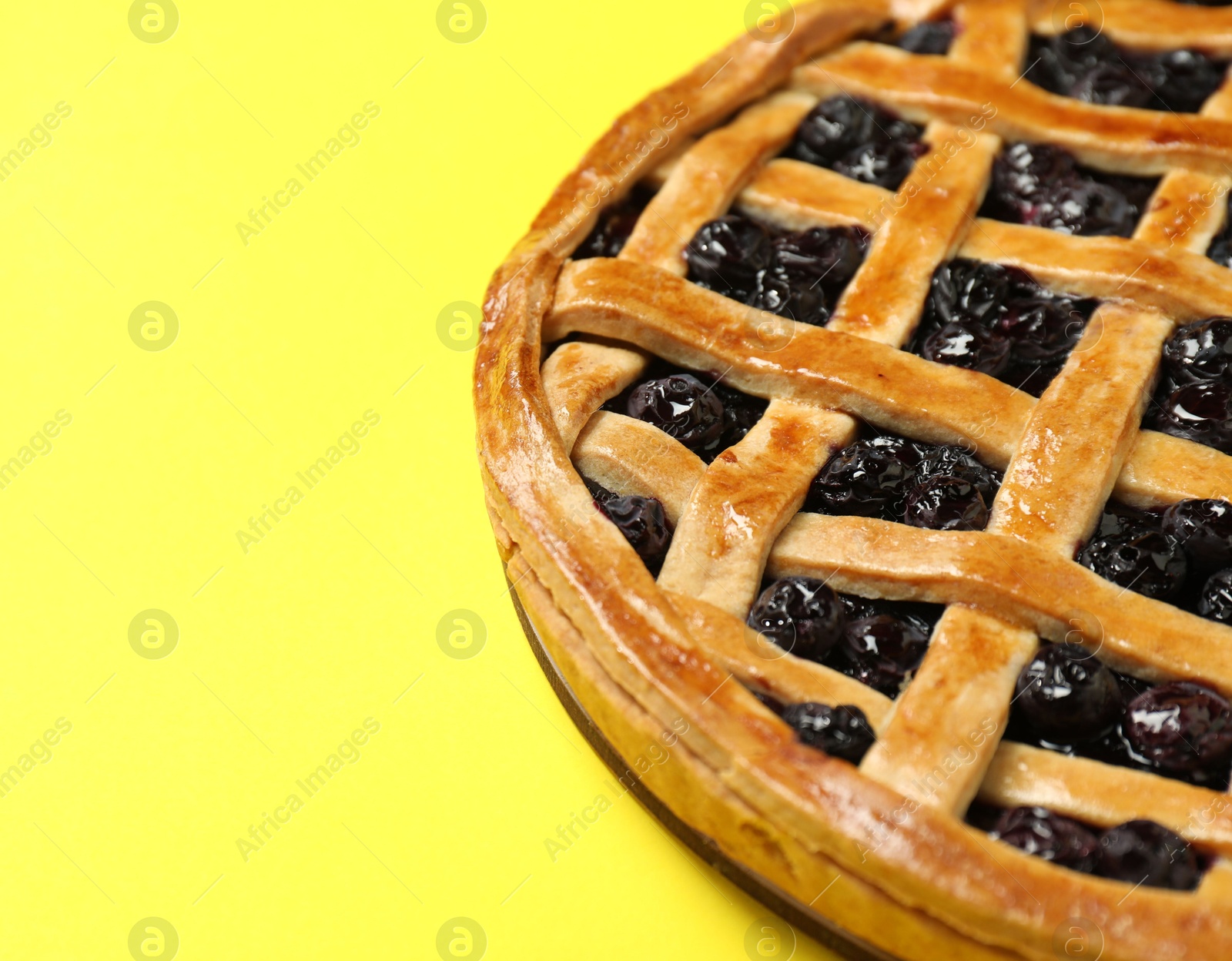 Photo of Tasty homemade pie with blueberries on yellow table, closeup. Space for text