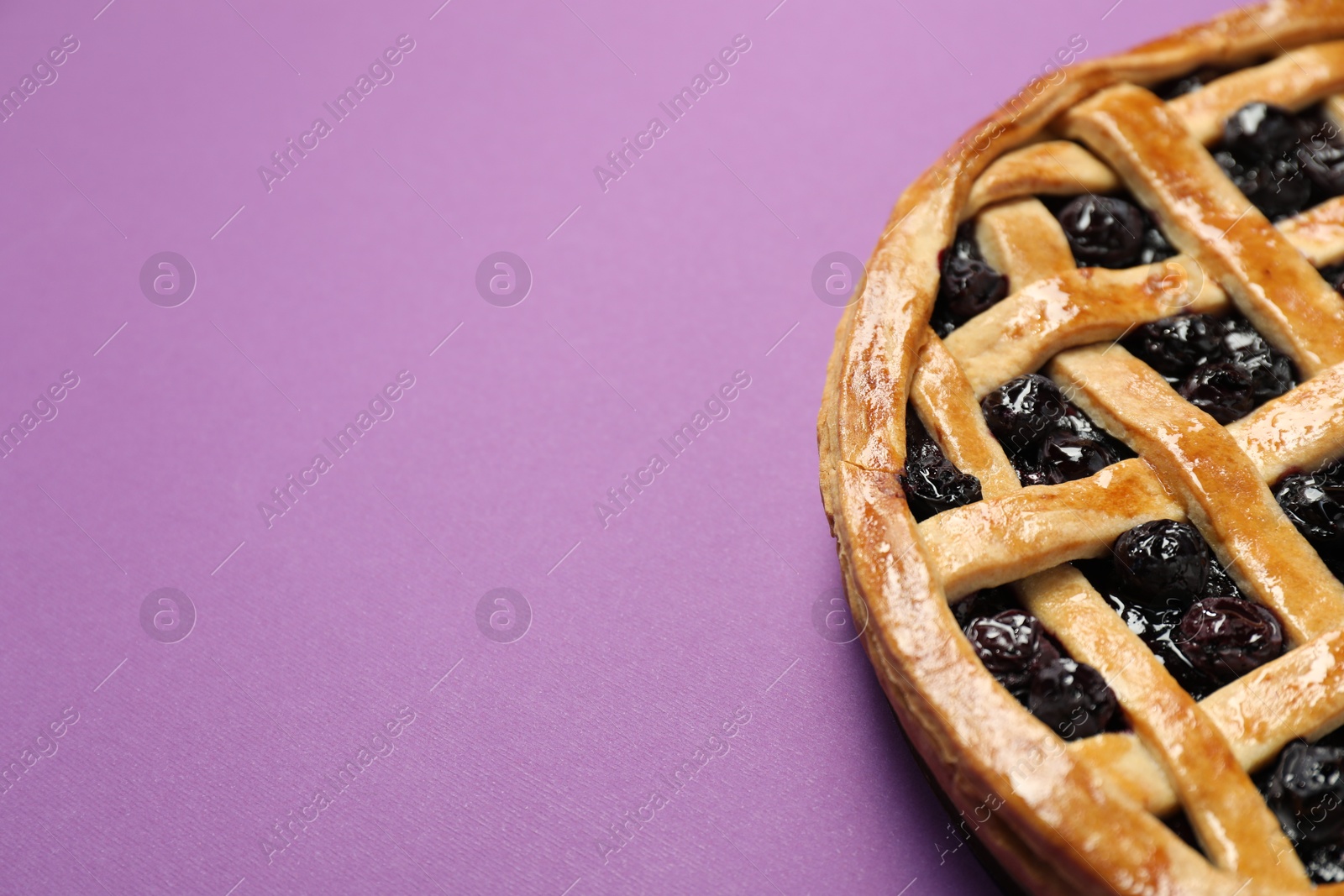 Photo of Tasty homemade pie with blueberries on purple table, closeup. Space for text