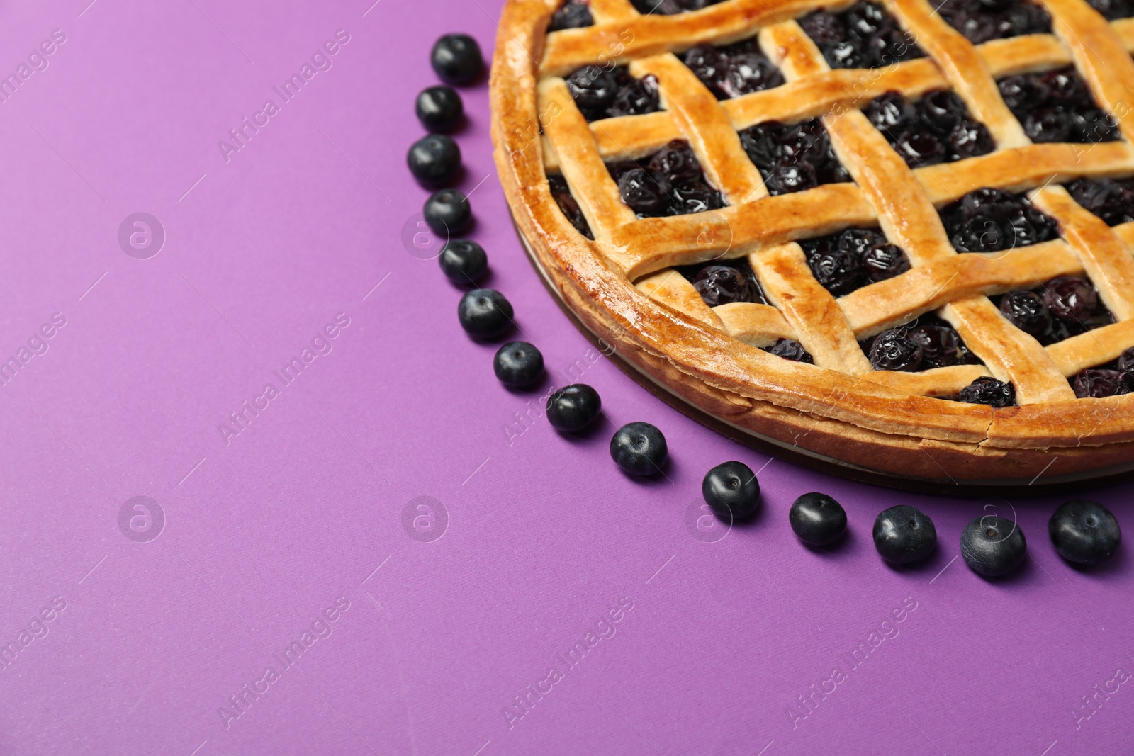 Photo of Tasty homemade pie with blueberries on purple table, closeup. Space for text