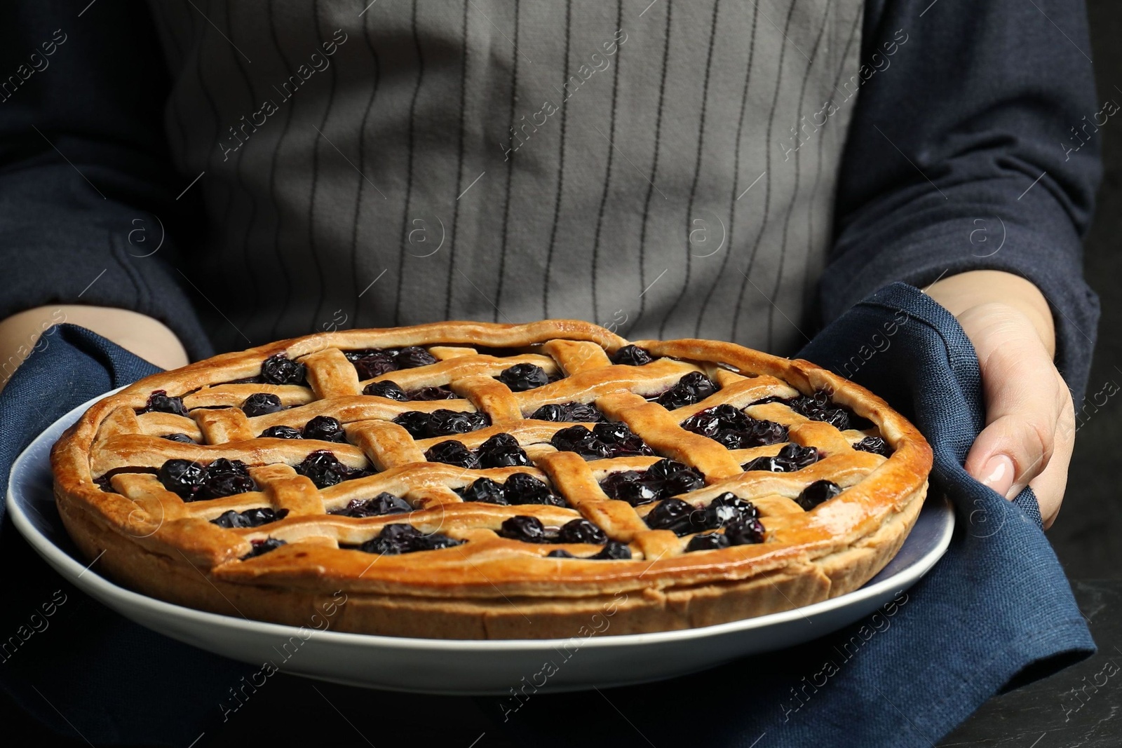 Photo of Woman holding tasty homemade pie with blueberries over table, closeup