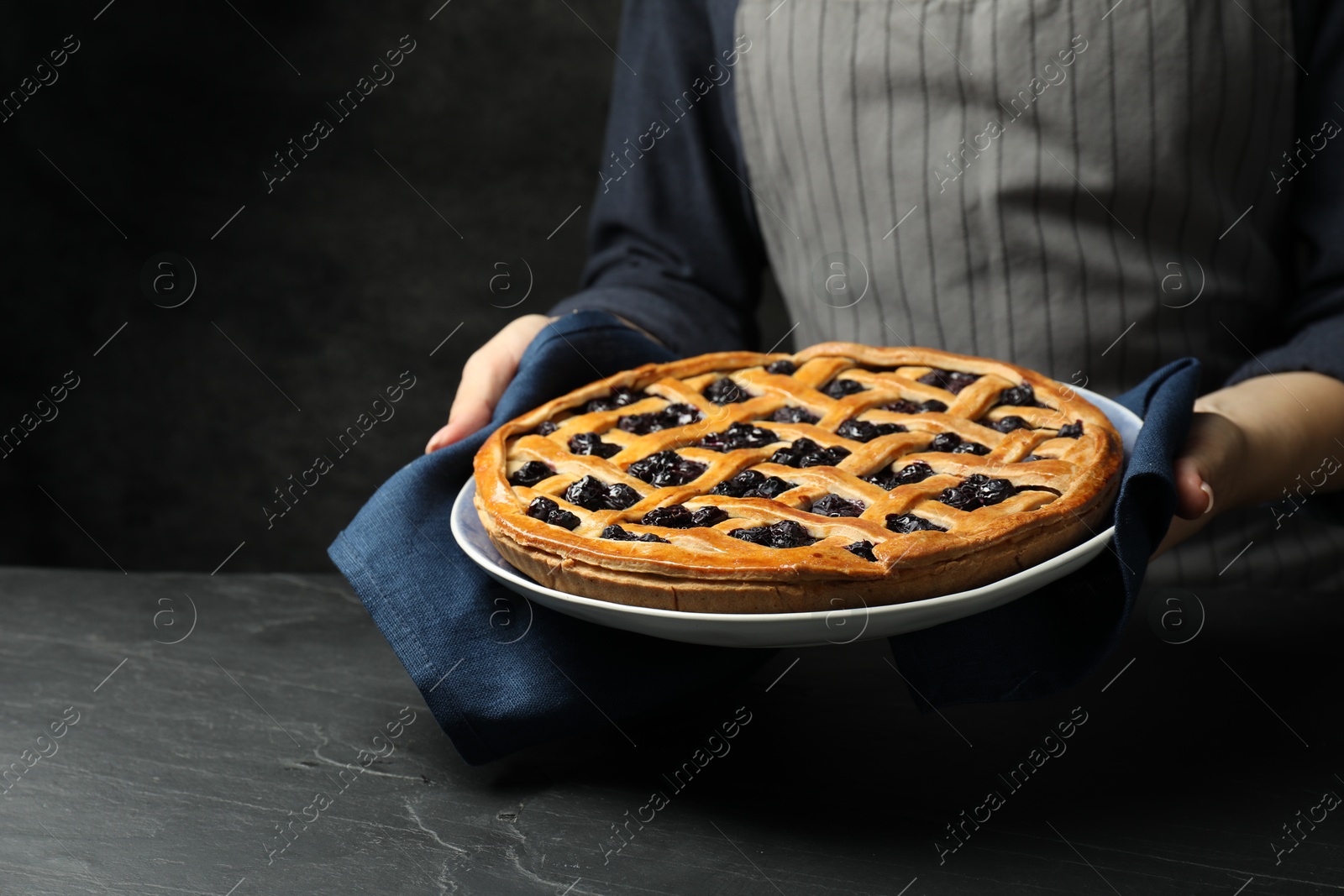 Photo of Woman holding tasty homemade pie with blueberries over grey textured table, closeup