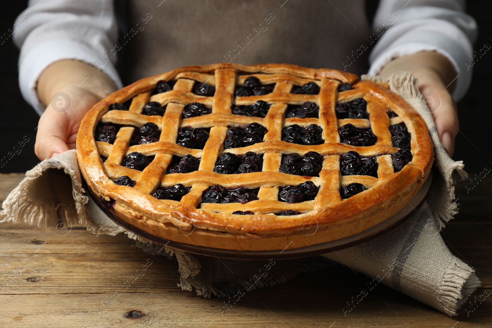 Photo of Woman holding tasty homemade pie with blueberries over wooden table, closeup