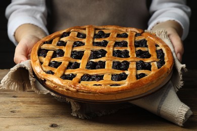 Photo of Woman holding tasty homemade pie with blueberries over wooden table, closeup