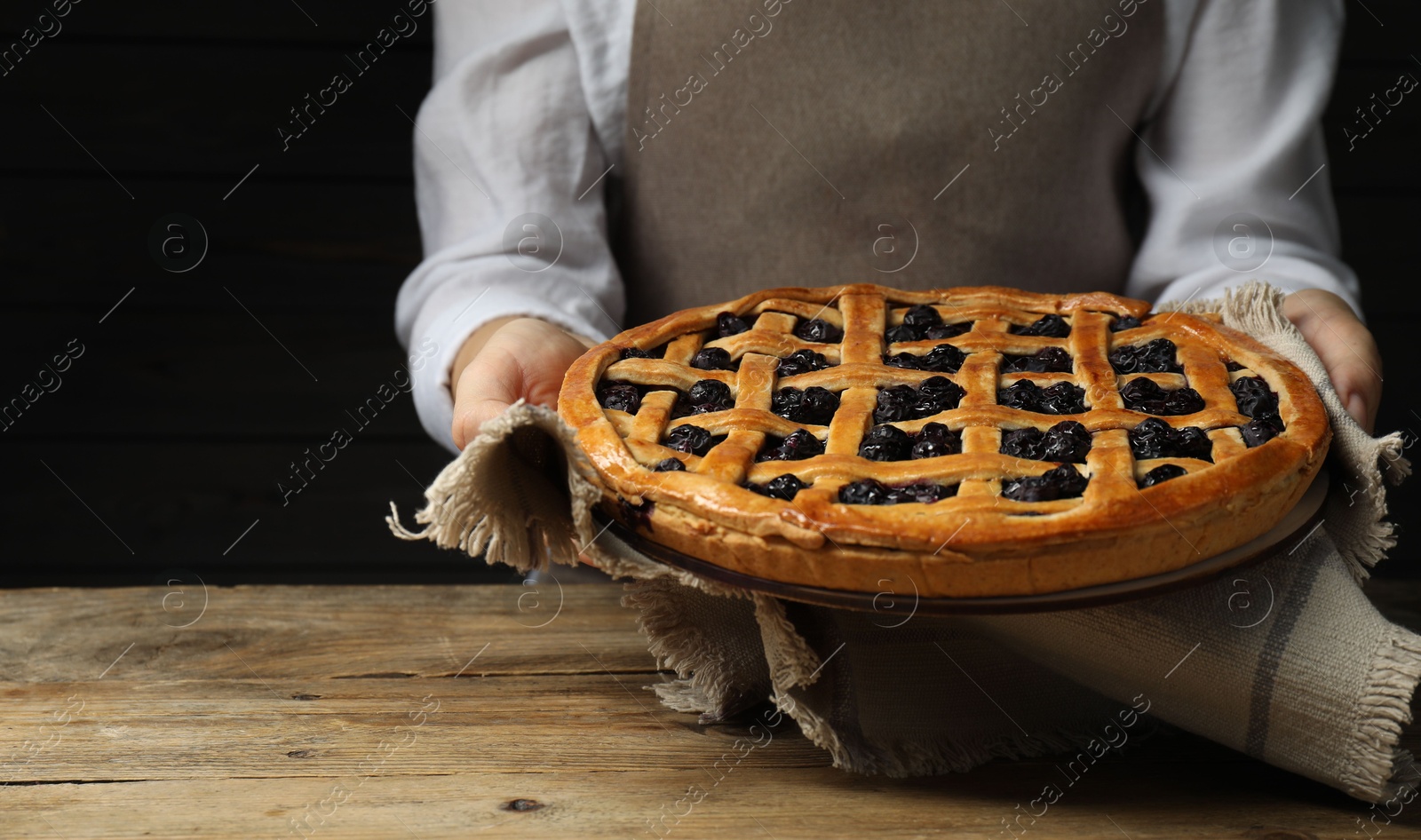 Photo of Woman holding tasty homemade pie with blueberries over wooden table, closeup