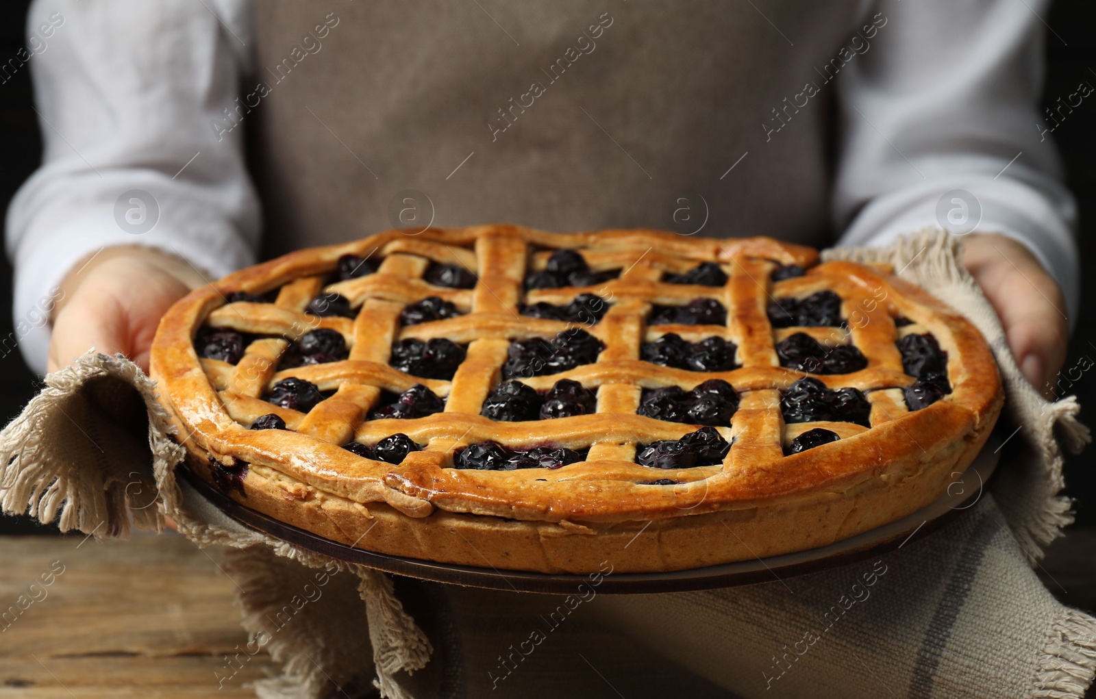 Photo of Woman holding tasty homemade pie with blueberries over wooden table, closeup