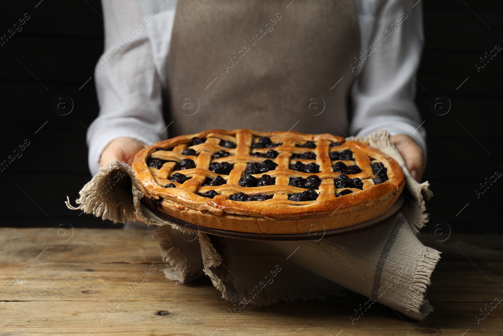 Photo of Woman holding tasty homemade pie with blueberries over wooden table, closeup