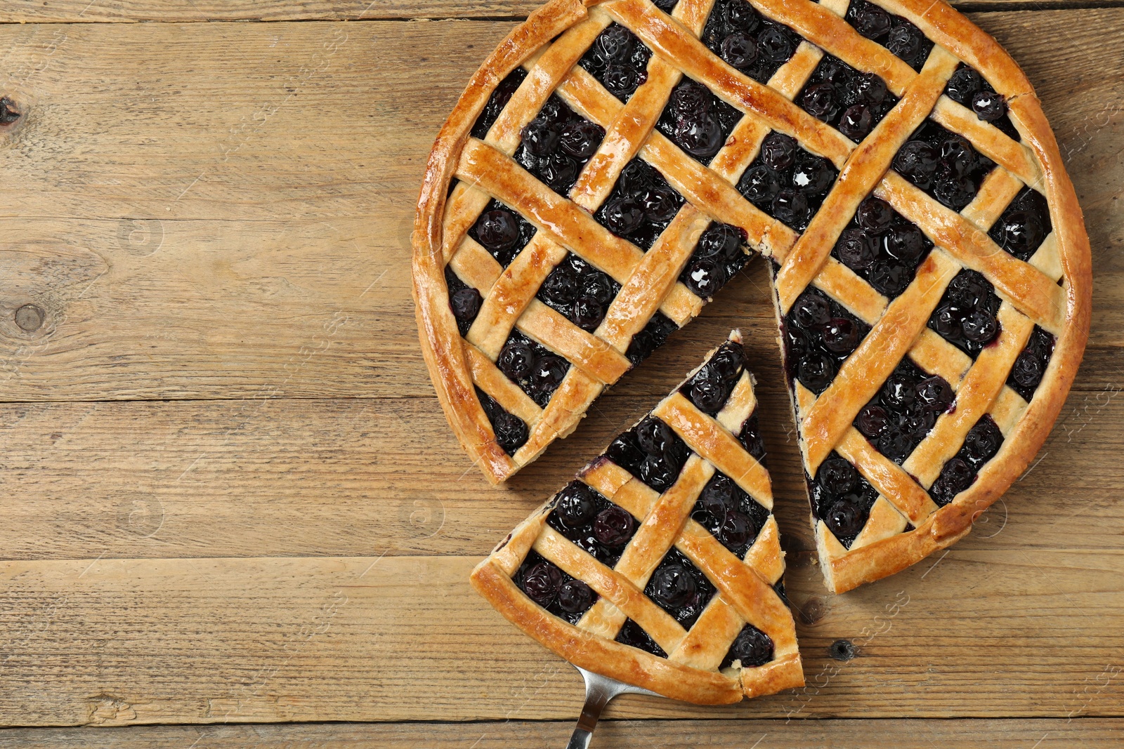 Photo of Taking piece of delicious homemade blueberry pie with server on wooden table, top view. Space for text