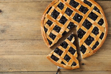 Photo of Taking piece of delicious homemade blueberry pie with server on wooden table, top view. Space for text