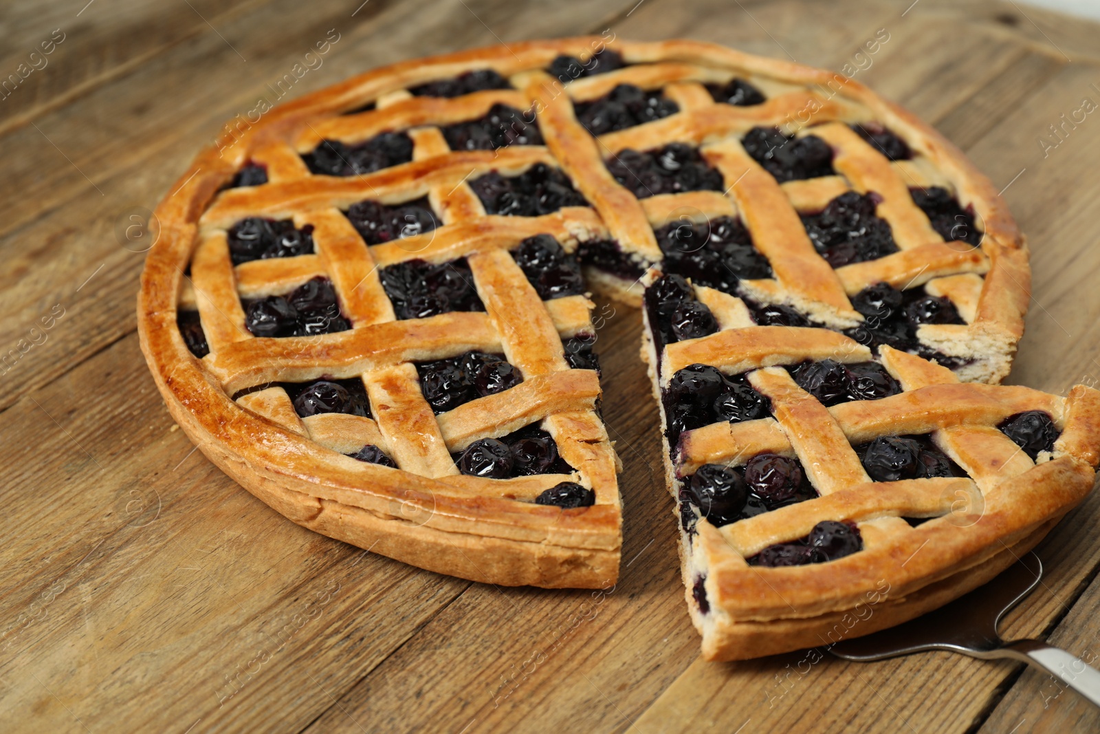 Photo of Taking piece of delicious homemade blueberry pie with server on wooden table