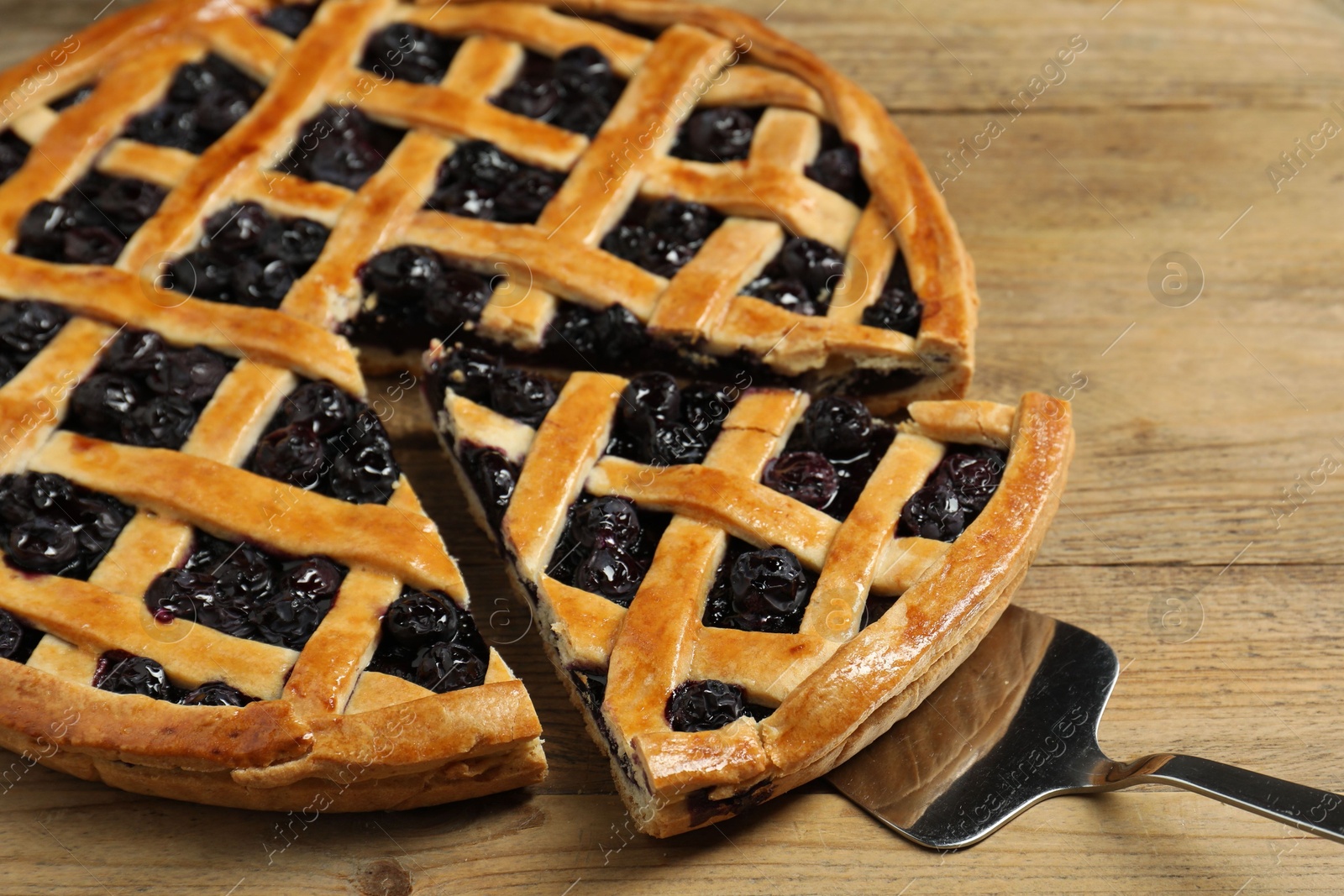 Photo of Taking piece of delicious homemade blueberry pie with server on wooden table, closeup