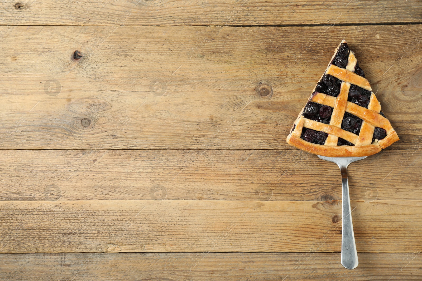 Photo of Piece of tasty homemade blueberry pie and server on wooden table, top view. Space for text