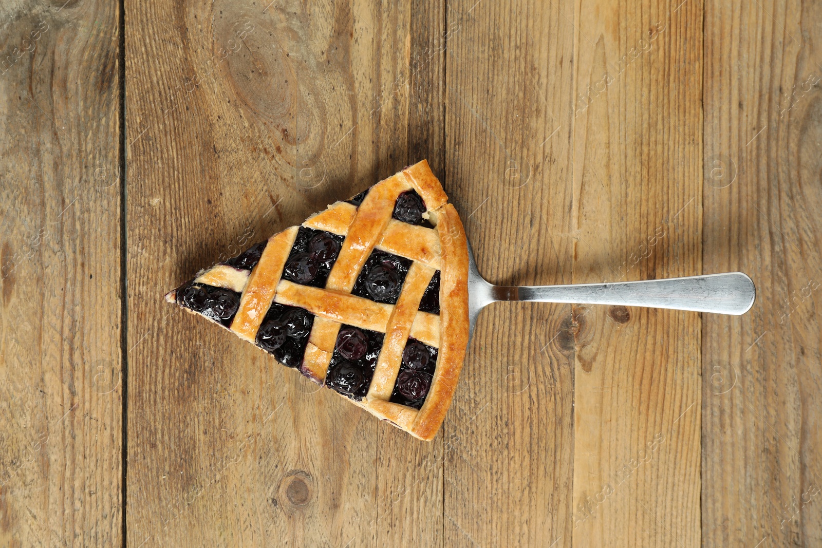 Photo of Piece of tasty homemade blueberry pie and server on wooden table, top view