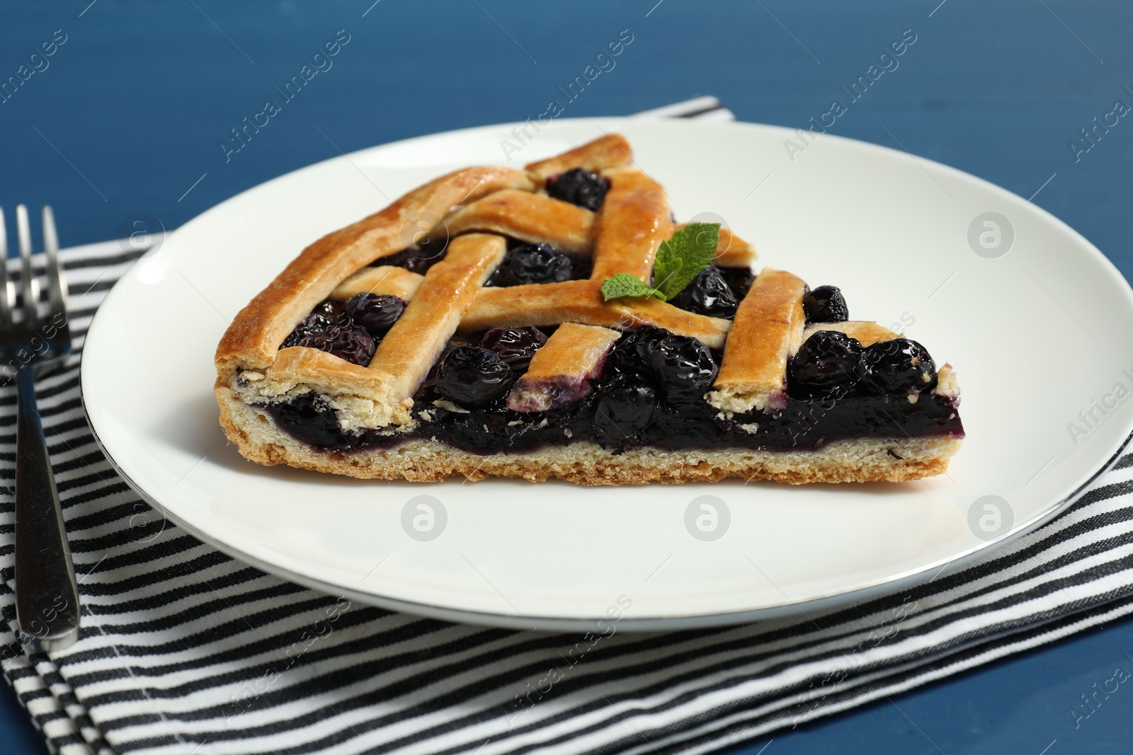 Photo of Piece of tasty homemade pie with blueberries served on blue table, closeup