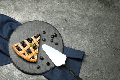 Photo of Piece of tasty homemade pie with blueberries and server on grey textured table, flat lay