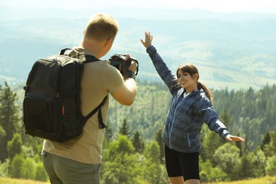 Photographer with backpack and camera taking picture of model in beautiful mountains, back view