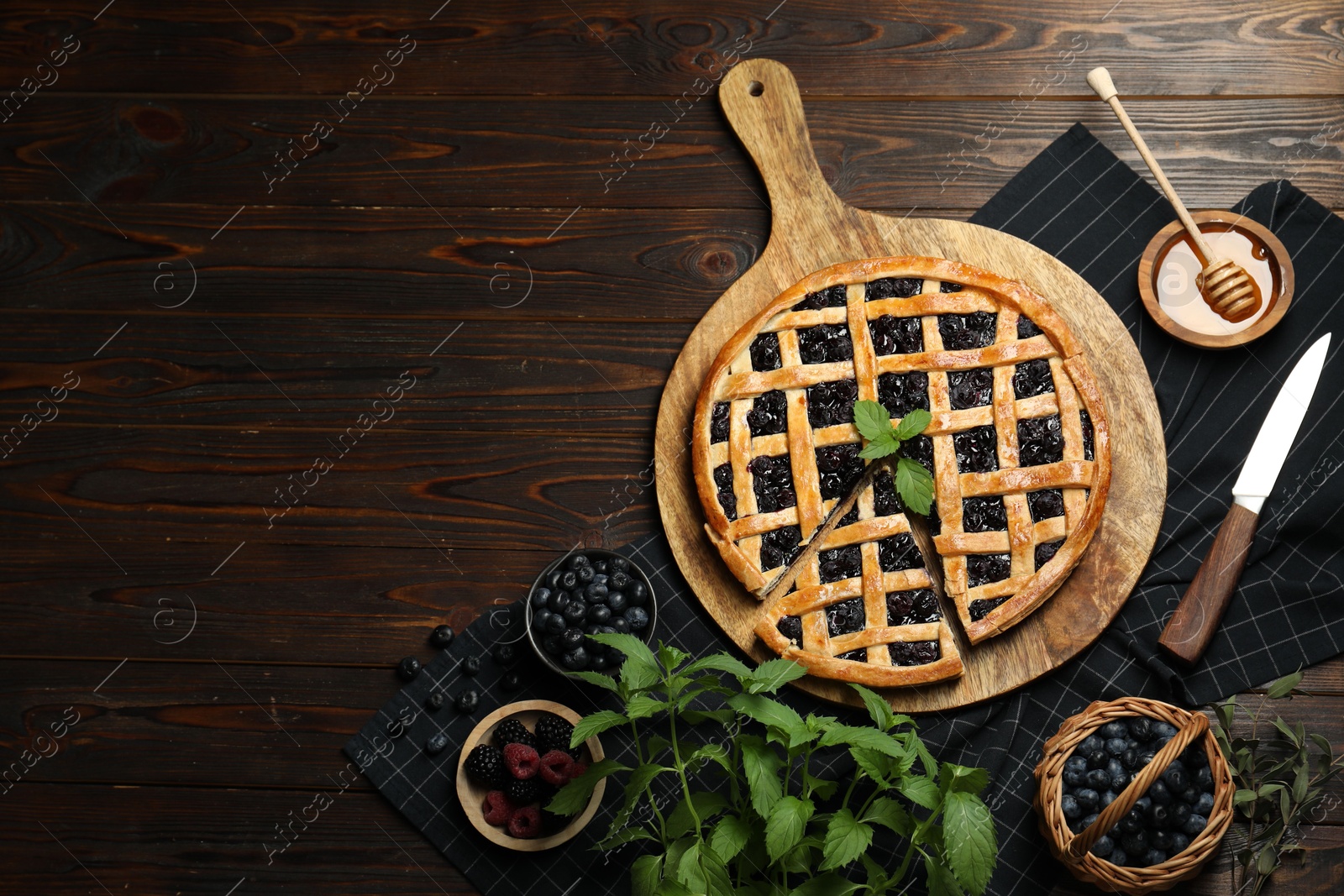 Photo of Tasty homemade pie with blueberries, fresh berries, mint, honey and knife on wooden table, flat lay. Space for text