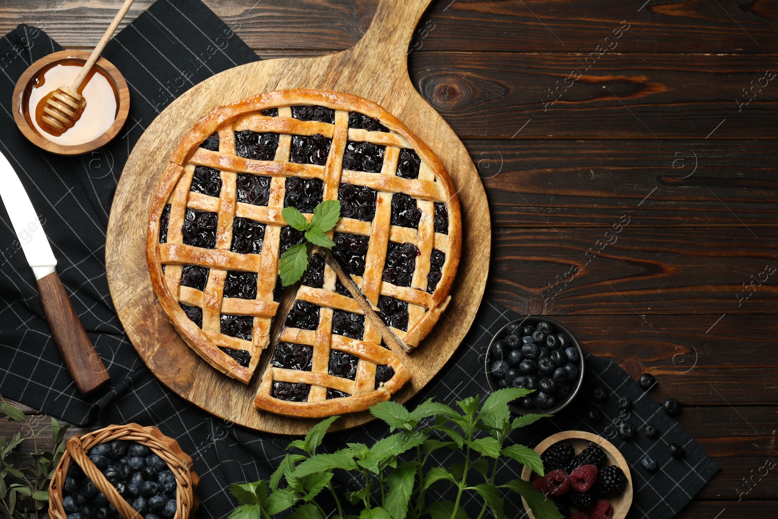 Photo of Tasty homemade pie with blueberries, fresh berries, mint, honey and knife on wooden table, flat lay. Space for text