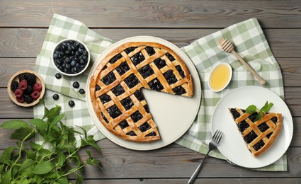 Photo of Tasty homemade pie with blueberries, fresh berries, mint, honey and fork on wooden table, flat lay