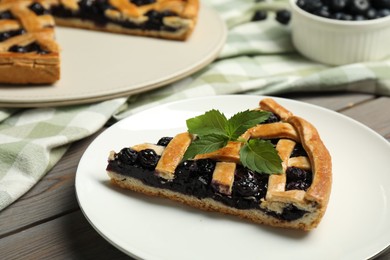 Photo of Piece of tasty homemade pie with blueberries and mint on table, closeup