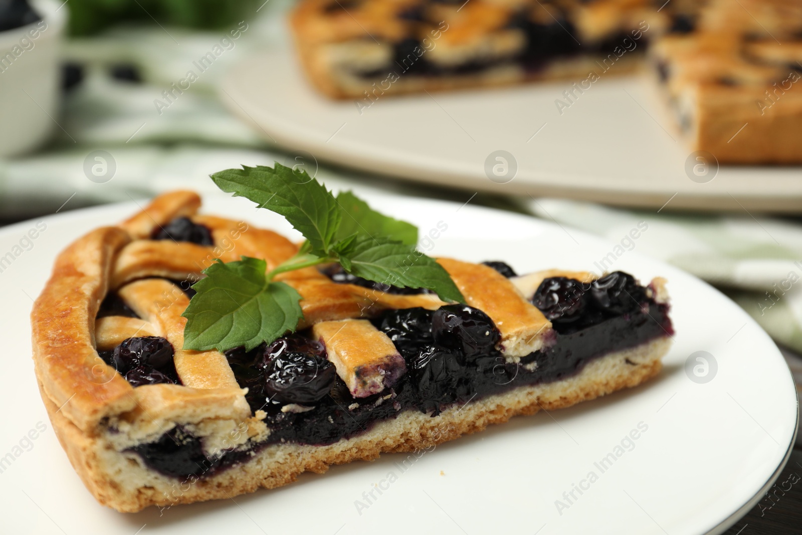 Photo of Piece of tasty homemade pie with blueberries and mint on table, closeup