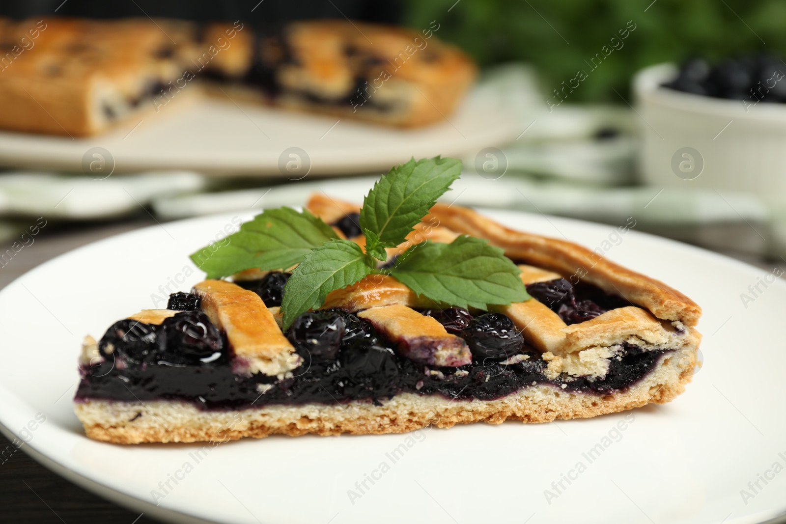 Photo of Piece of tasty homemade pie with blueberries and mint on table, closeup