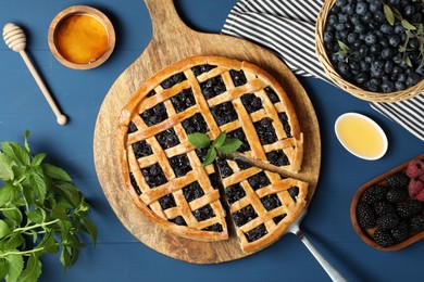 Photo of Tasty homemade pie with blueberries, fresh berries, mint, honey and cake server on blue wooden table, flat lay