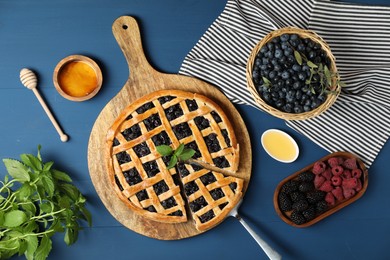 Photo of Tasty homemade pie with blueberries, fresh berries, mint, honey and cake server on blue wooden table, flat lay