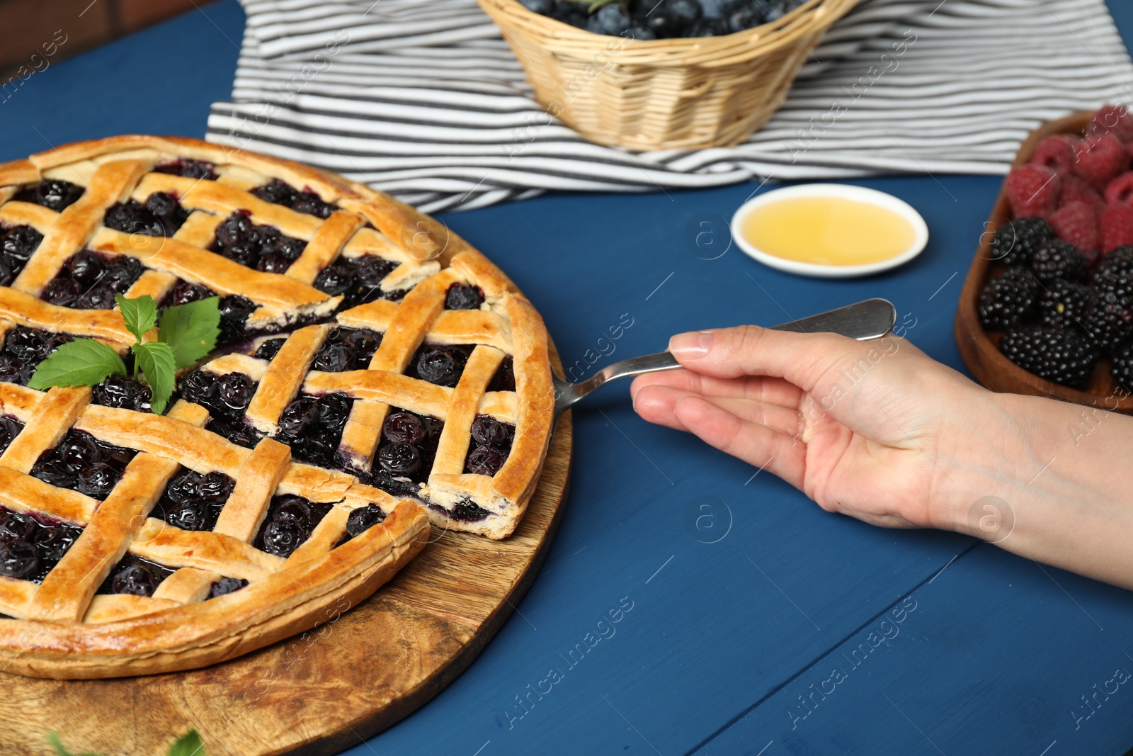 Photo of Woman taking piece of tasty homemade pie with blueberries at blue wooden table, closeup