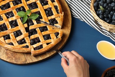 Photo of Woman taking piece of tasty homemade pie with blueberries at blue wooden table, above view