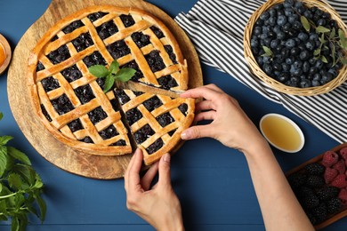 Photo of Woman taking piece of tasty homemade pie with blueberries at blue wooden table, top view