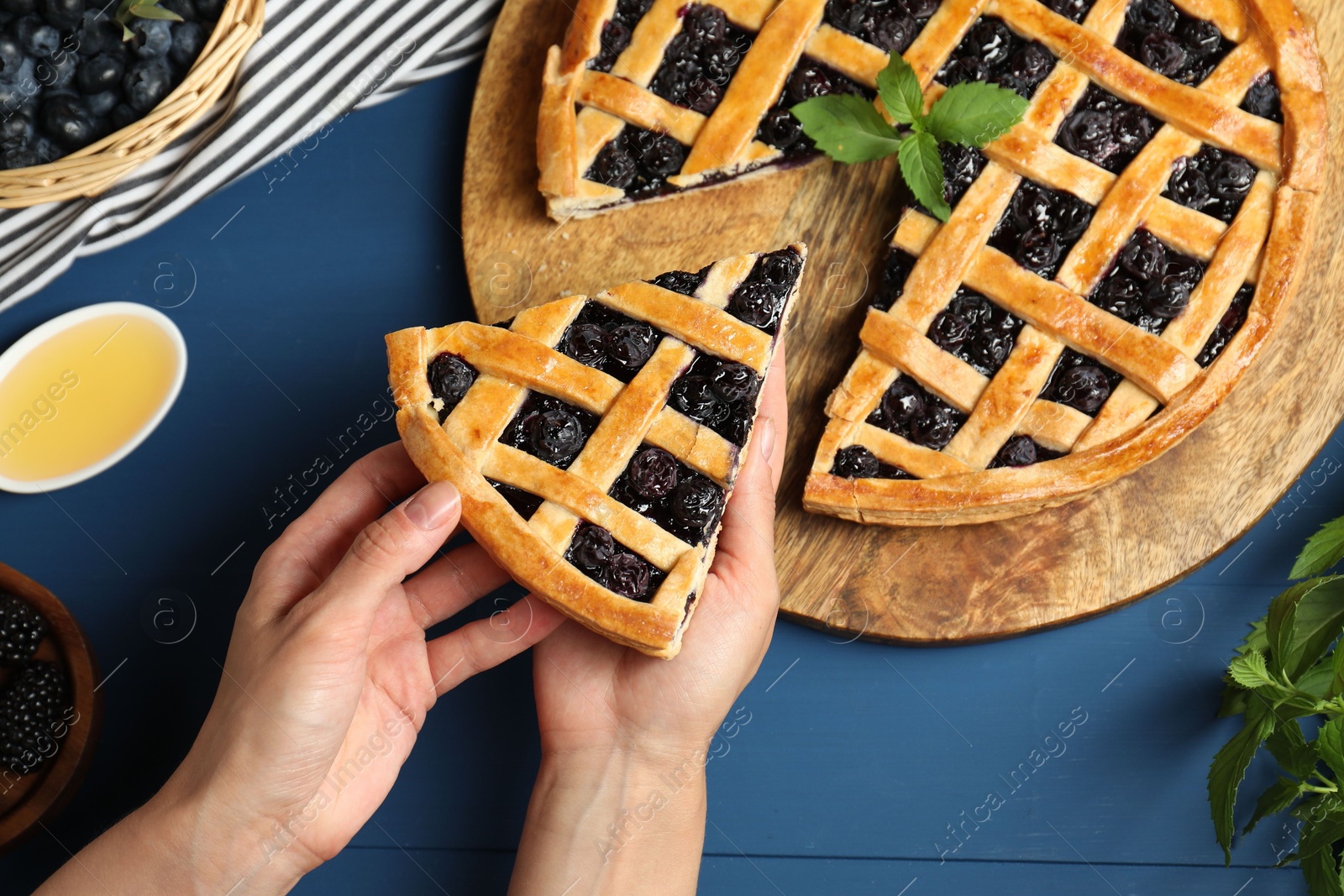 Photo of Woman taking piece of tasty homemade pie with blueberries at blue wooden table, top view