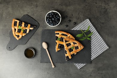 Photo of Pieces of tasty homemade pie with blueberries, mint and honey on gray textured table, flat lay