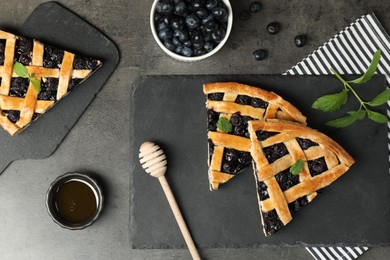 Photo of Pieces of tasty homemade pie with blueberries, mint and honey on gray textured table, flat lay