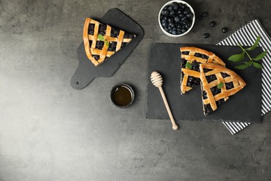 Photo of Pieces of tasty homemade pie with blueberries, mint and honey on gray textured table, flat lay. Space for text