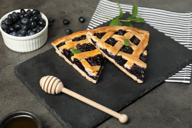 Photo of Pieces of tasty homemade pie with blueberries, mint and honey dipper on gray textured table