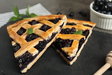 Pieces of tasty homemade pie with blueberries and mint on gray table, closeup