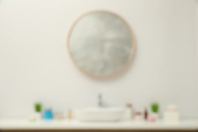 Photo of Blurred view of countertop with sink, houseplants and mirror in bathroom