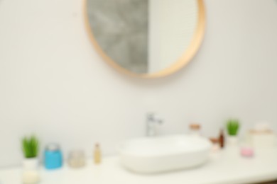 Photo of Blurred view of countertop with sink, houseplants and mirror in bathroom