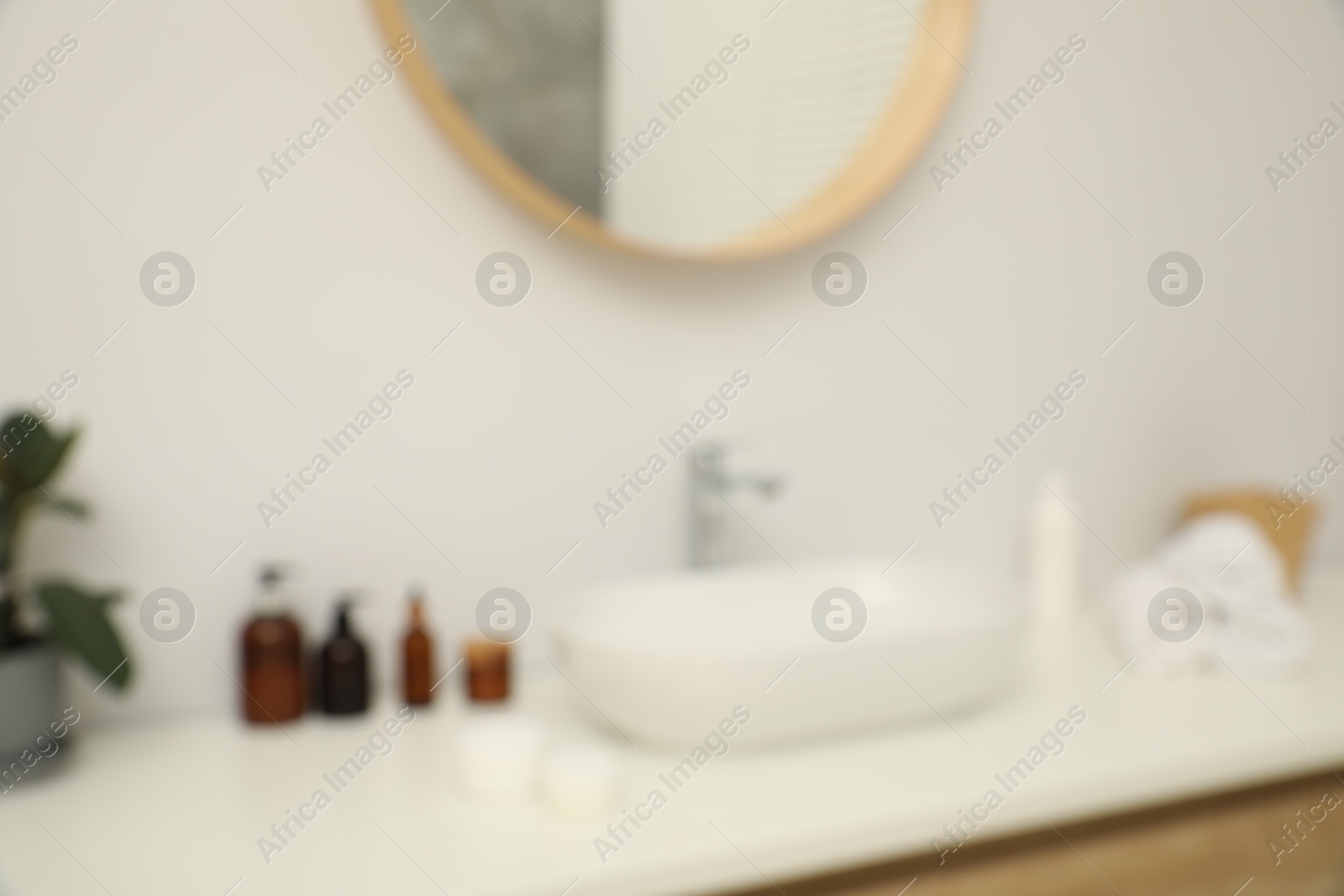 Photo of Blurred view of countertop with sink, towels, houseplant and mirror in bathroom