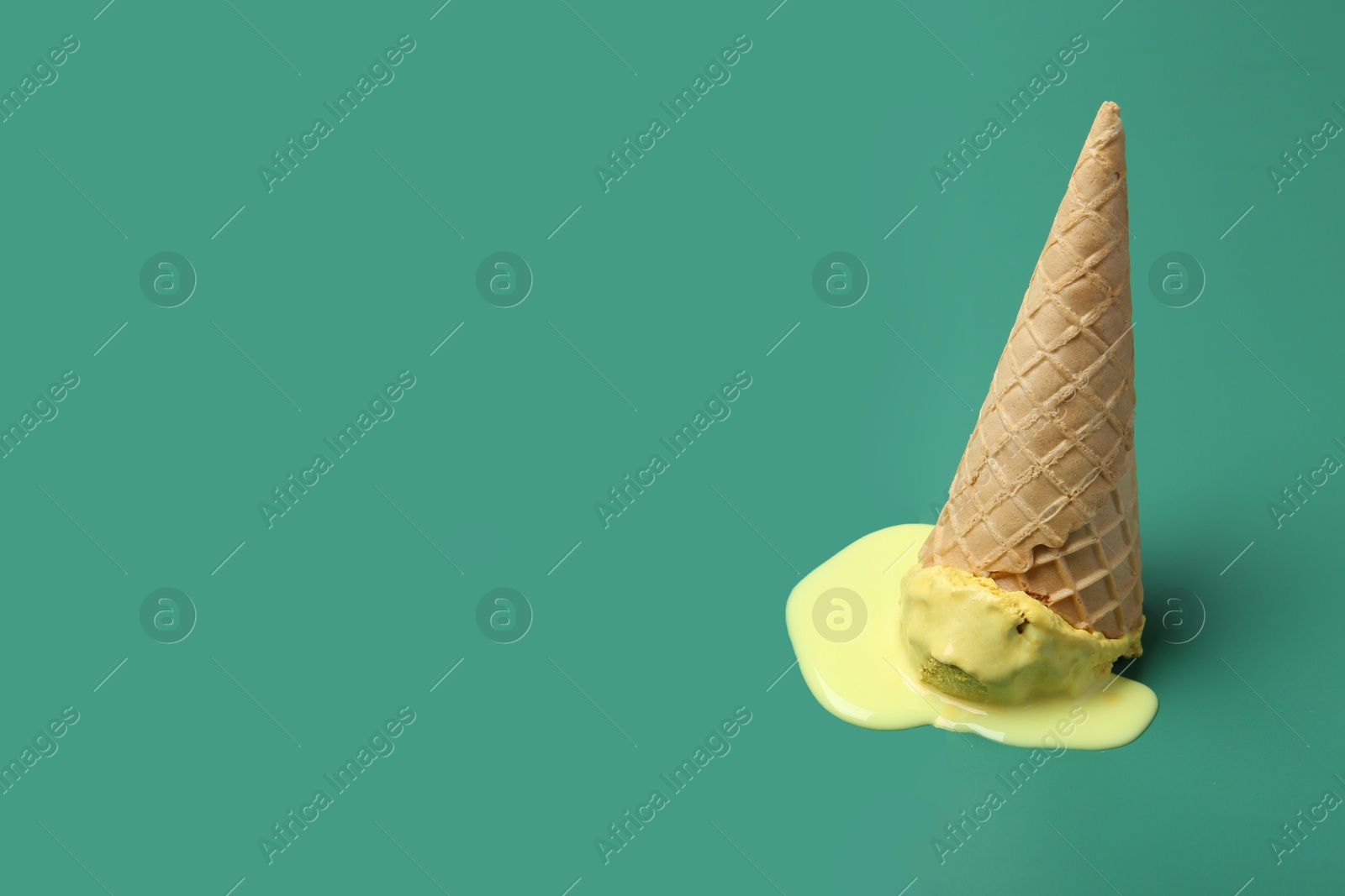 Photo of Melted ice cream in wafer cone on pale green background. Space for text