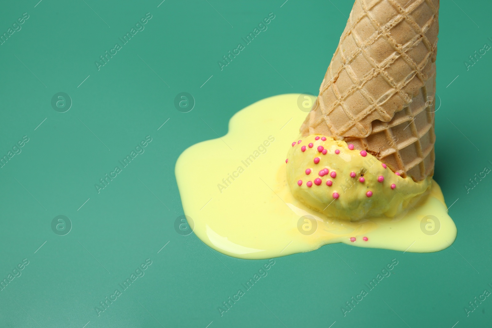 Photo of Melted ice cream in wafer cone on pale green background, closeup. Space for text