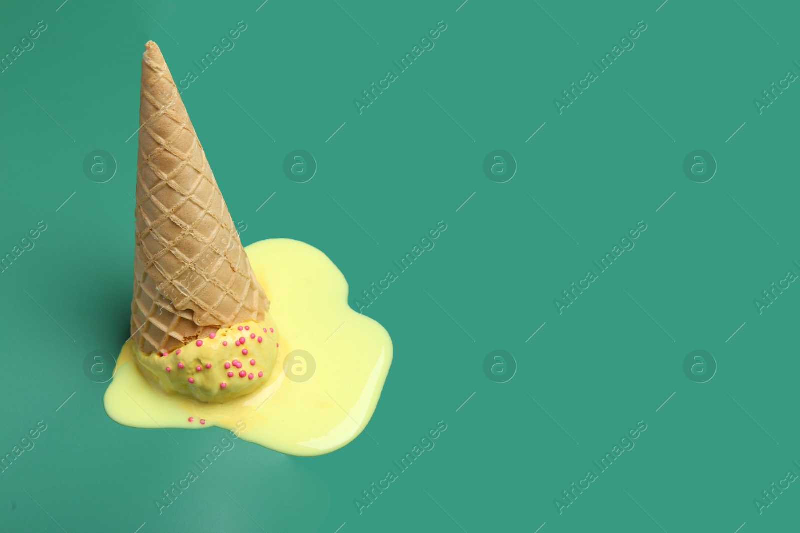 Photo of Melted ice cream in wafer cone on pale green background. Space for text