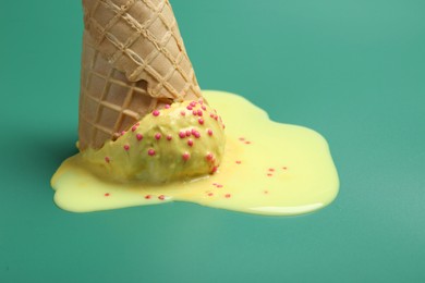 Photo of Melted ice cream in wafer cone on pale green background, closeup