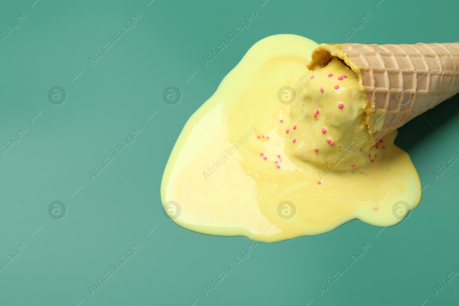 Photo of Melted ice cream in wafer cone on pale green background. Space for text