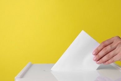 Woman putting her vote into ballot box against yellow background, closeup. Space for text